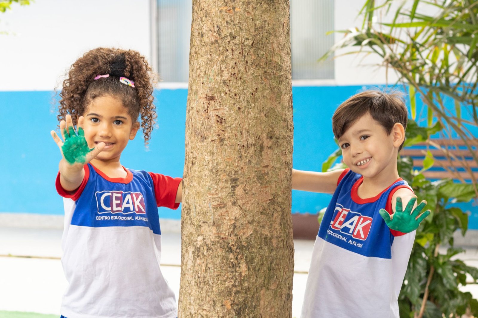 Duas crianças sorrindo ao lado de uma árvore no pátio do CEAK